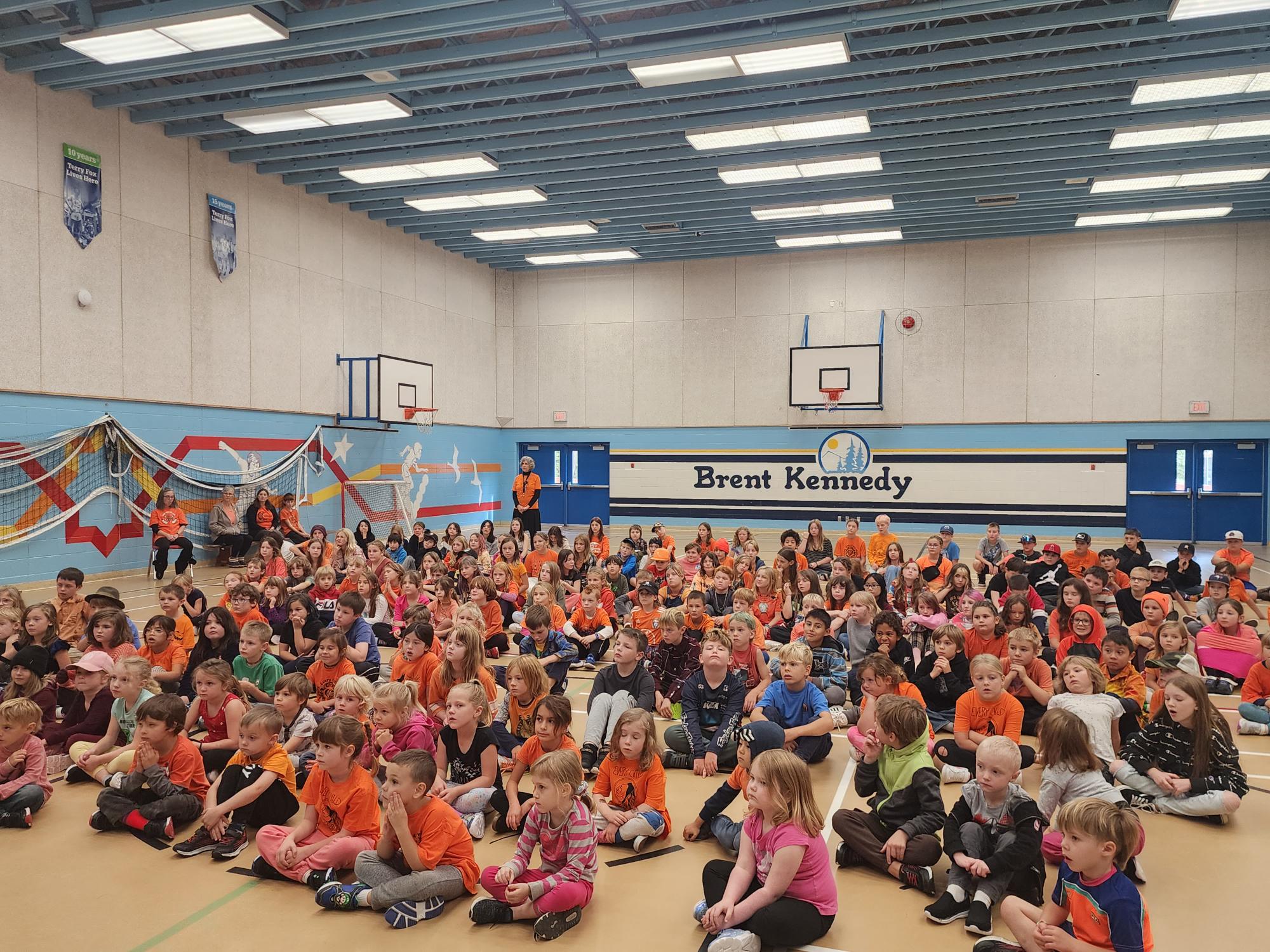 A group of children sitting on the floor in a gym</p>
<p>Description automatically generated
