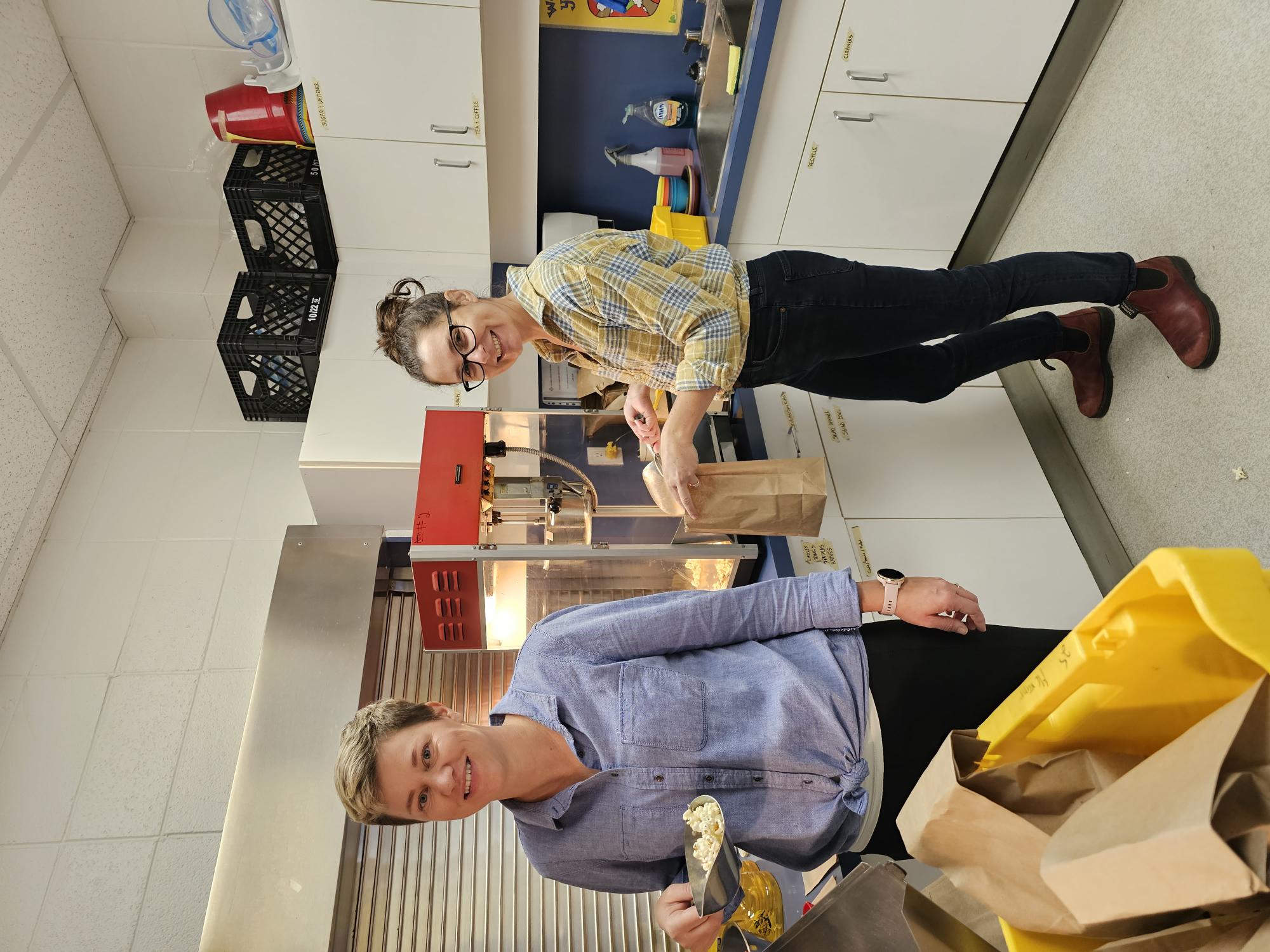 A person and person standing in a room with a counter and a bag of popcorn</p>
<p>Description automatically generated