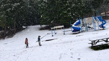 Two children in a snowy school playground beside the forest in winter