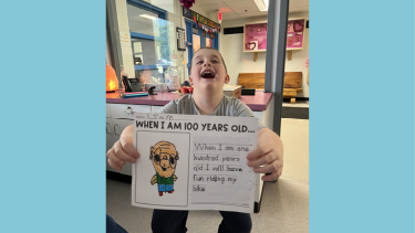 A boy laughs as he holds up a school project
