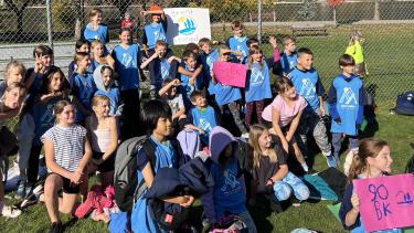 A group of elementary school students in a school field getting ready for a cross-country run on a sunny fall day