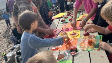 Children make candy apples around a wooden picnic table outdoors.