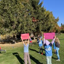 Students at an elementary school holding up pink signs from fellow students running in an x-country event